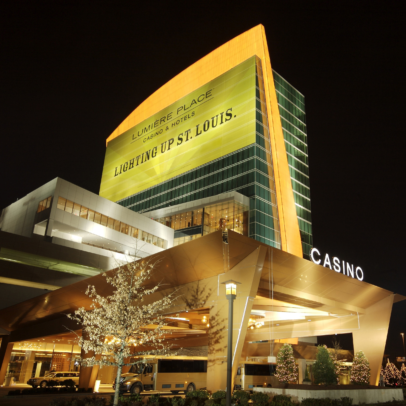 Lumiere Place Casino lit up at night. A sign on the side reads "Lumiere Place Casino & Hotels - Lighting Up St. Louis."