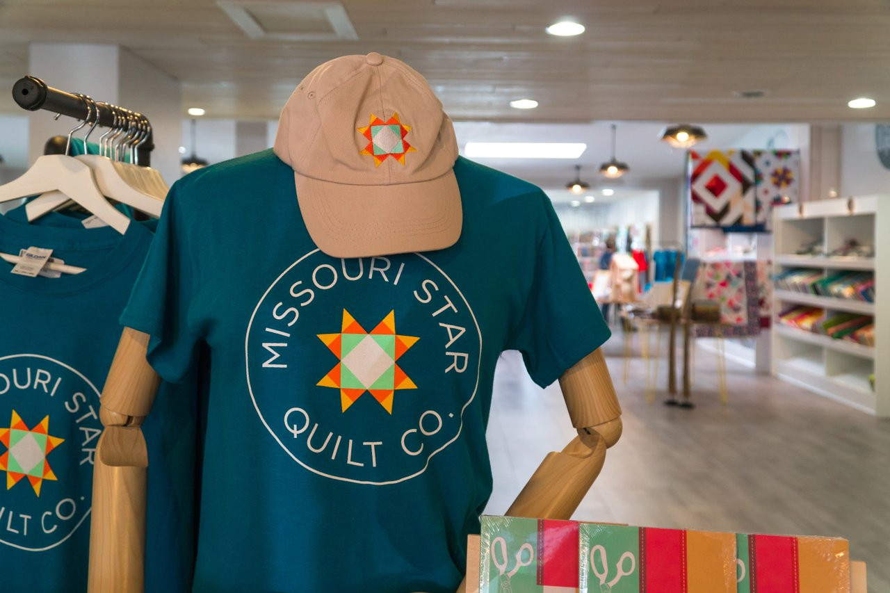 A mannequin in a brightly lit store wearing a hat and t-shirt with the Missouri Star Quilt Co. logo on them.