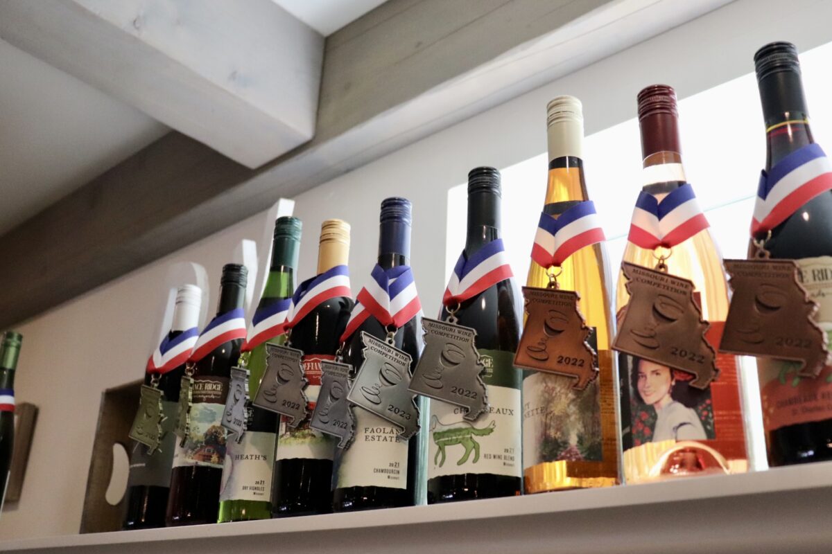 Bottles of wine sit on a shelf and each one has an awarded medal wrapped around it.