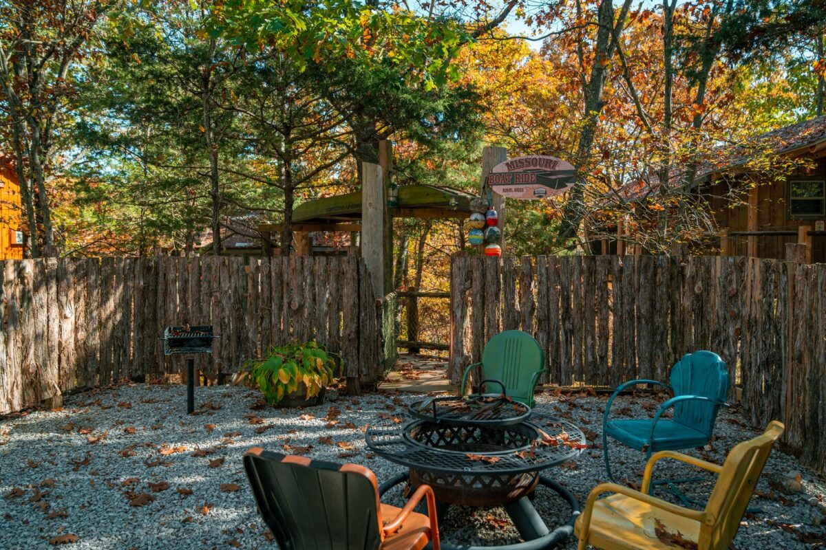 Lounge chair surround a firepit in a private, fenced-in area. Trees with fall foliage surround the private space.