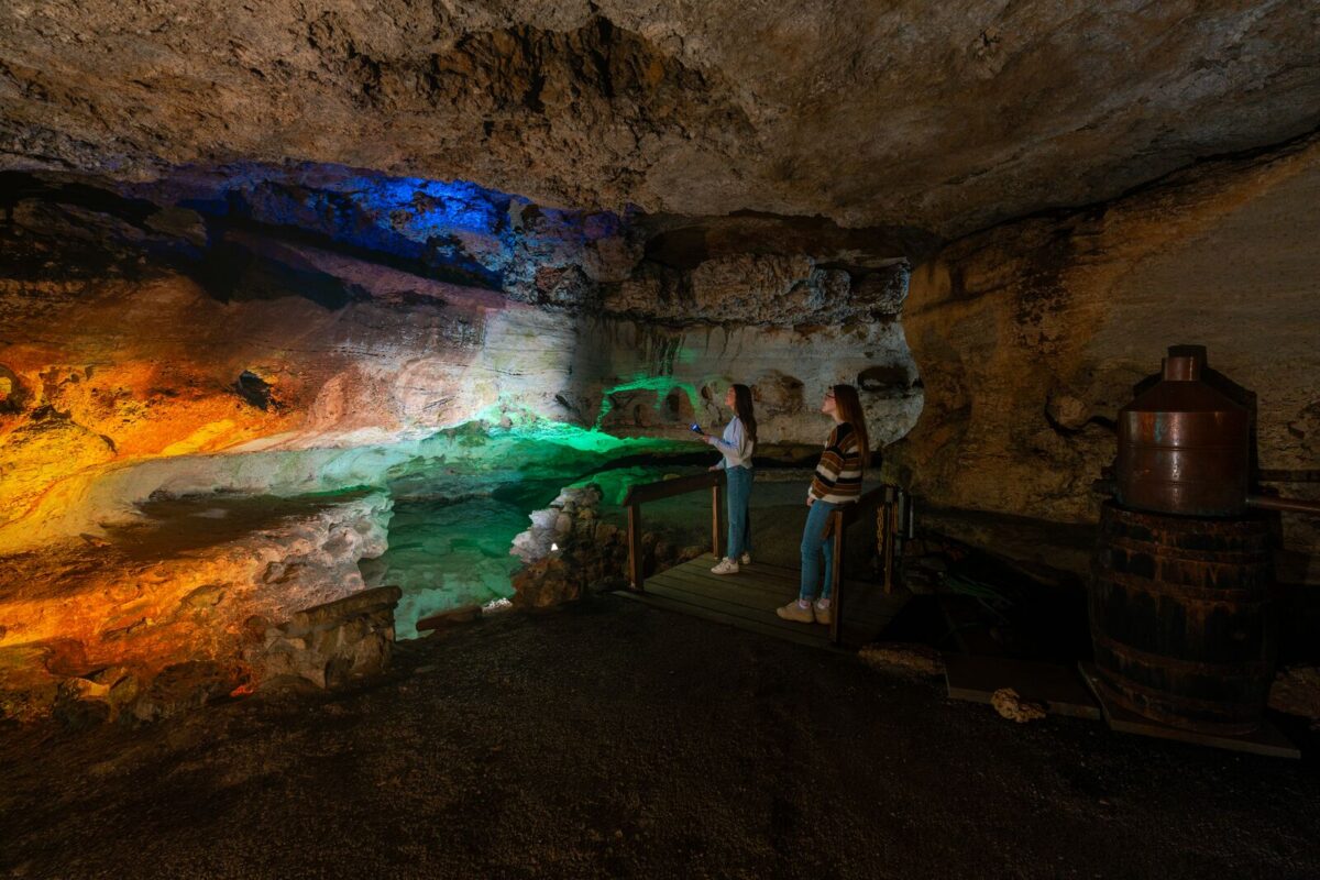 Two people look with a flashlight at the formations inside a cave.