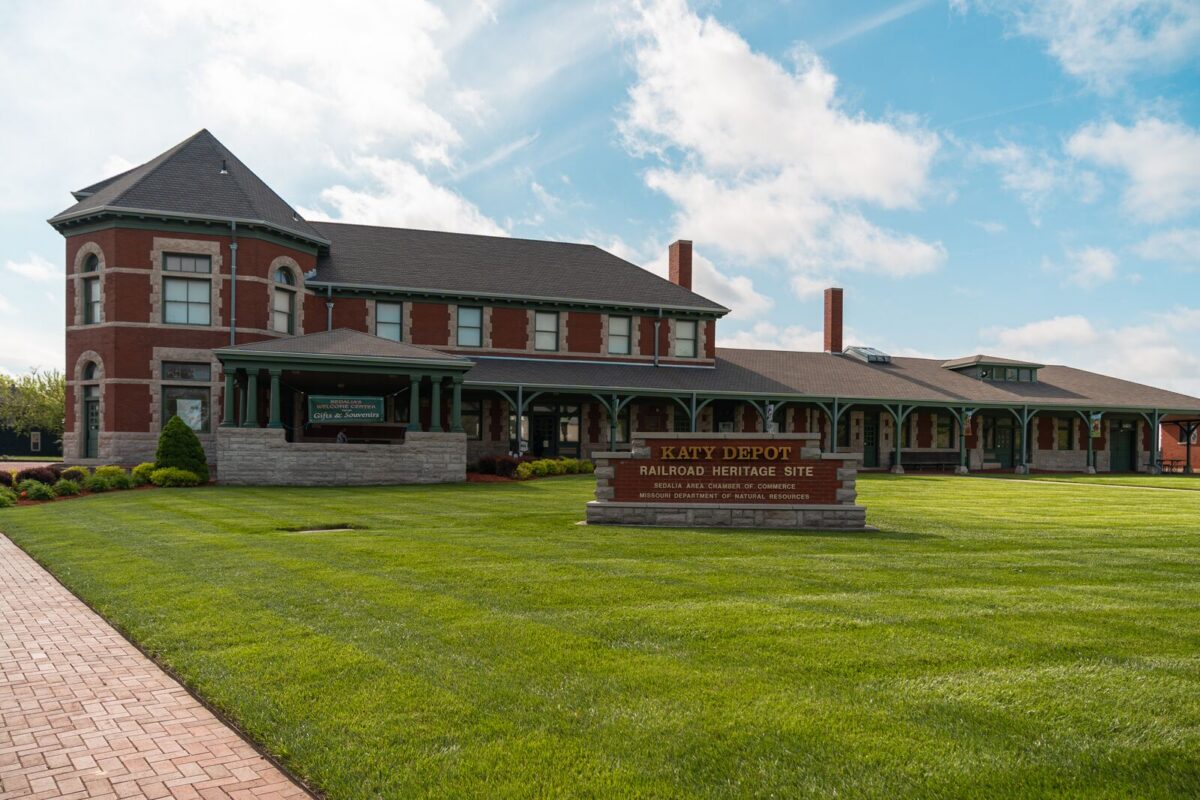 A large train depot sits on a bright lawn of green grass.