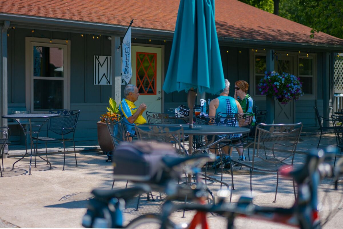 People sit at an iron table outside a bike shop. 
