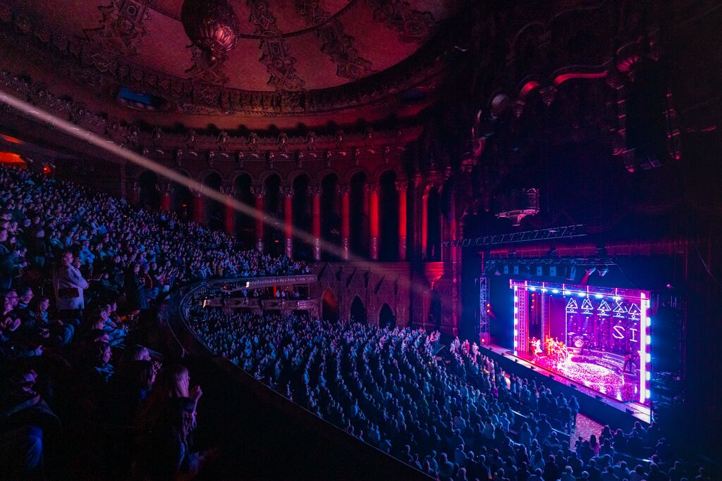 People sit in a large plush concert hall and enjoy music.
