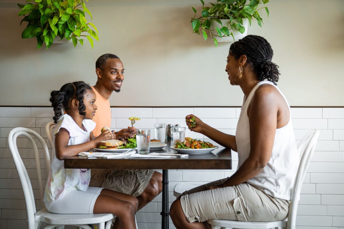 A family of three sit at a table over a meal. 