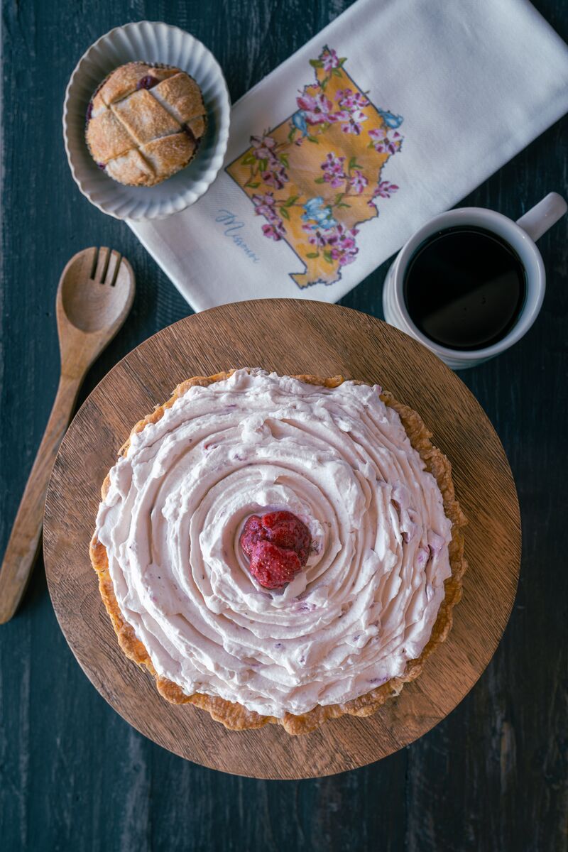 A light pink pie topped with a strawberry slice sits on a table with a wooden spoon.