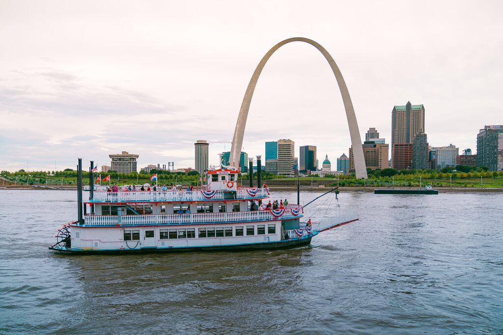A 19th-century replica river boat navigates the Mississippi River with a view of the St. Louis skyline.