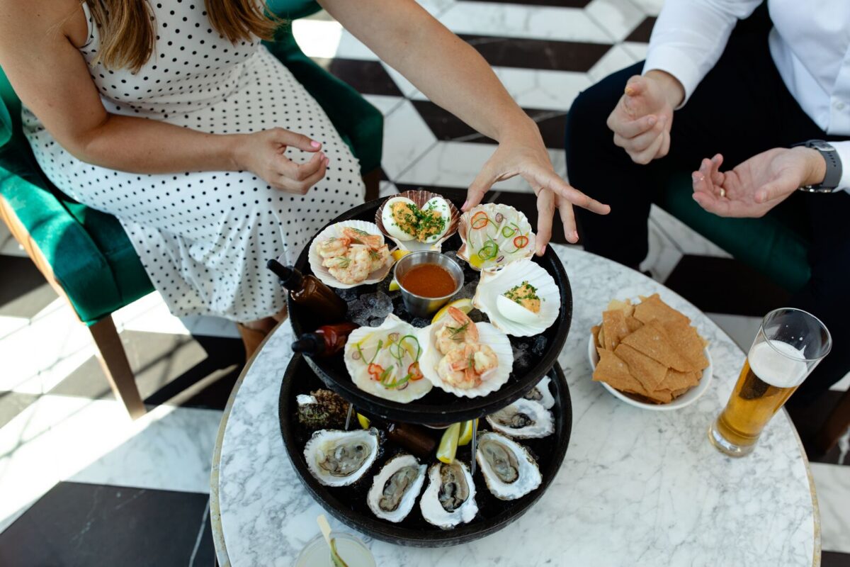 Two people sit at a small table with a two-tier serving tray of oysters and other appetizers.