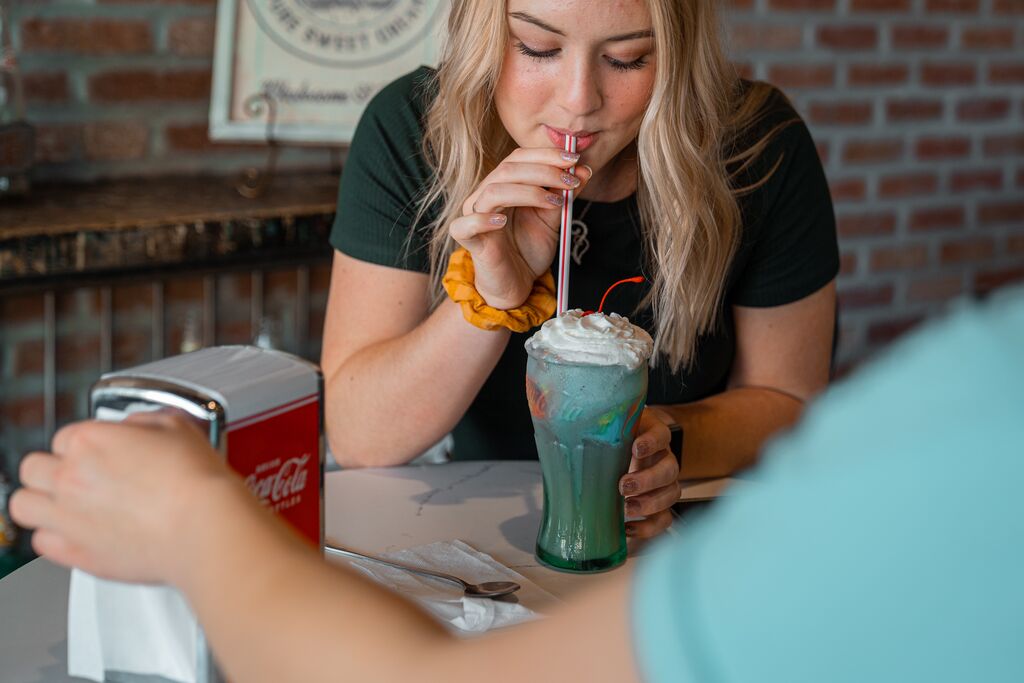 A person sips on a milkshake in a vintage glass.