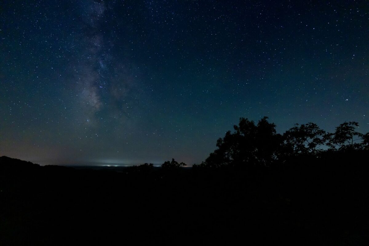 A dark landscape opens up to a beautiful night sky with the milky way present.