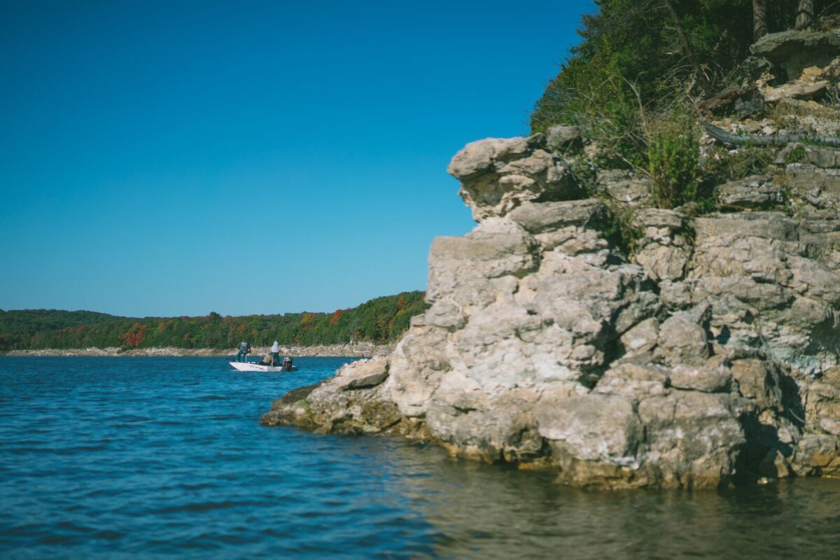 A boat sits on the water on a cool blue lake with a rock bluff in the foreground.