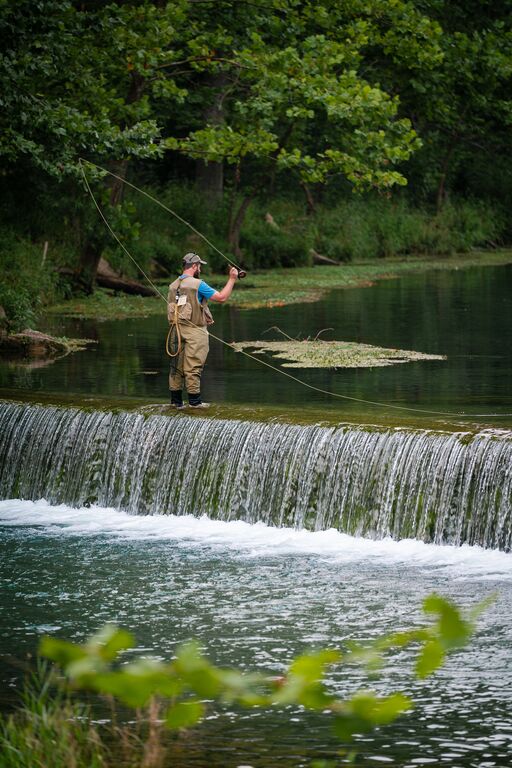 A person stands on a river dam and fly fishes. 