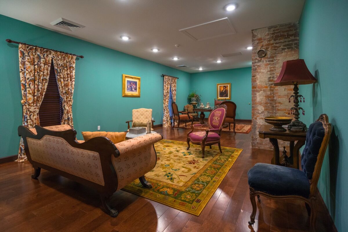 A warmly lit Victorian-style parlor belonging to the famous Missourian known as "Blind John" has teal walls, antique furniture and framed portraits. The room features an exposed brick column, brightly patterned area rugs and vintage chairs and lamps.
