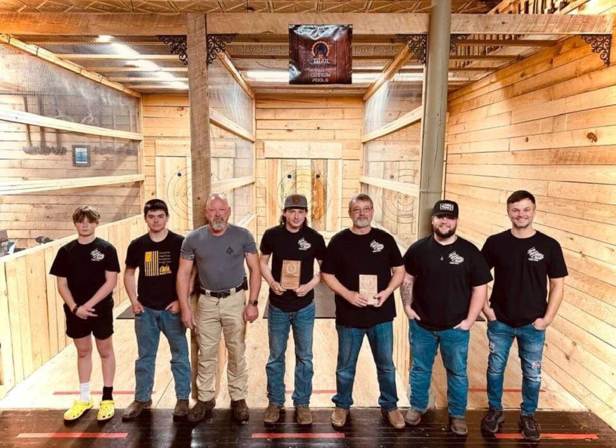 Several people pose in front of the lane of an axe throwing business.