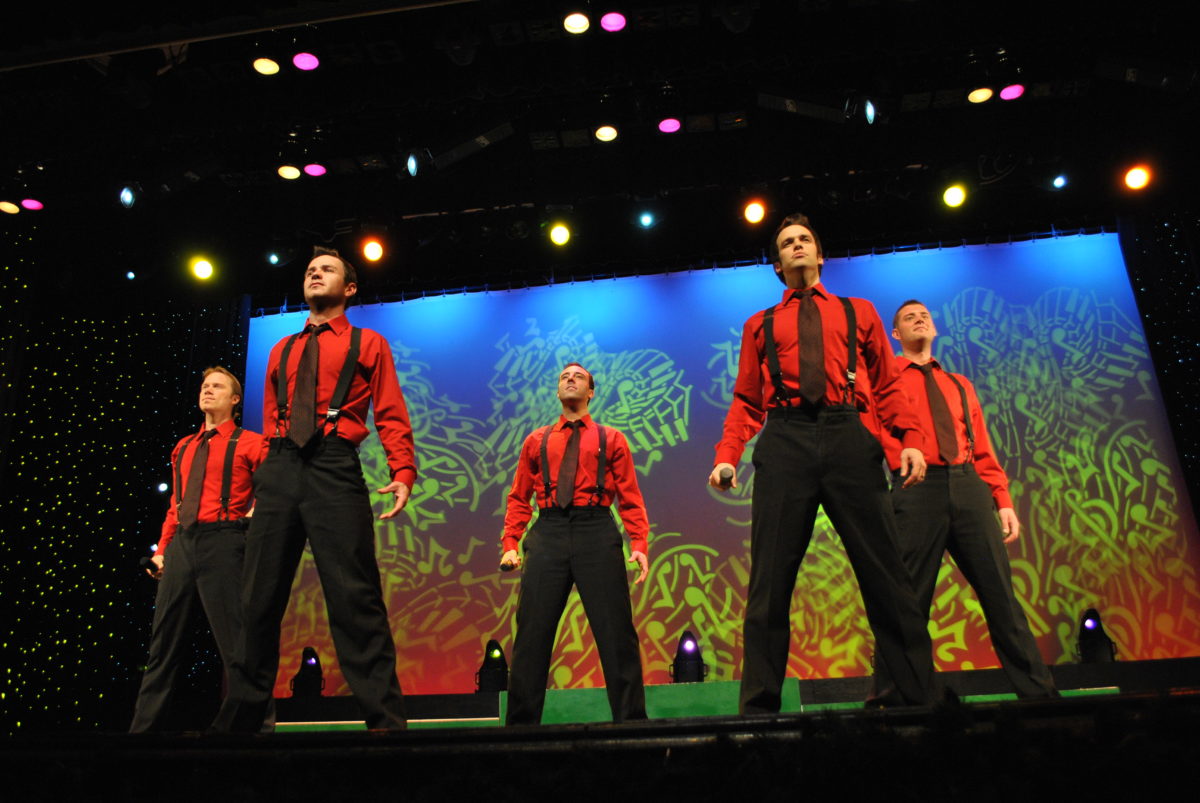 Five people in red shirts perform on stage.