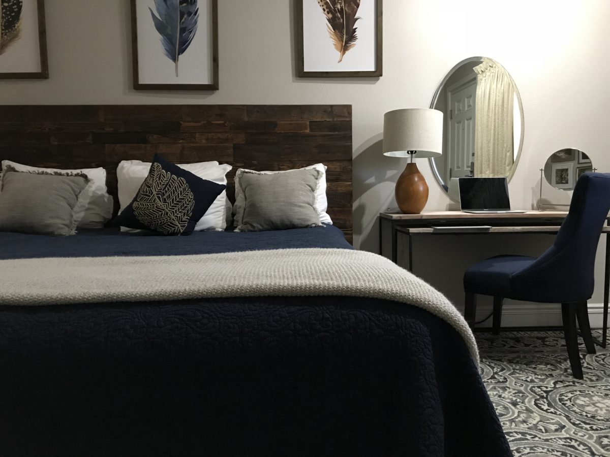 A made bed with cool colors and a stacked beside table with a chair.