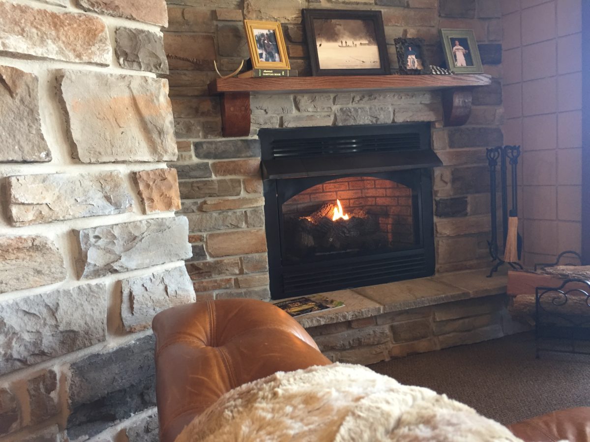 A sitting room with stone accents and a lit fireplace.
