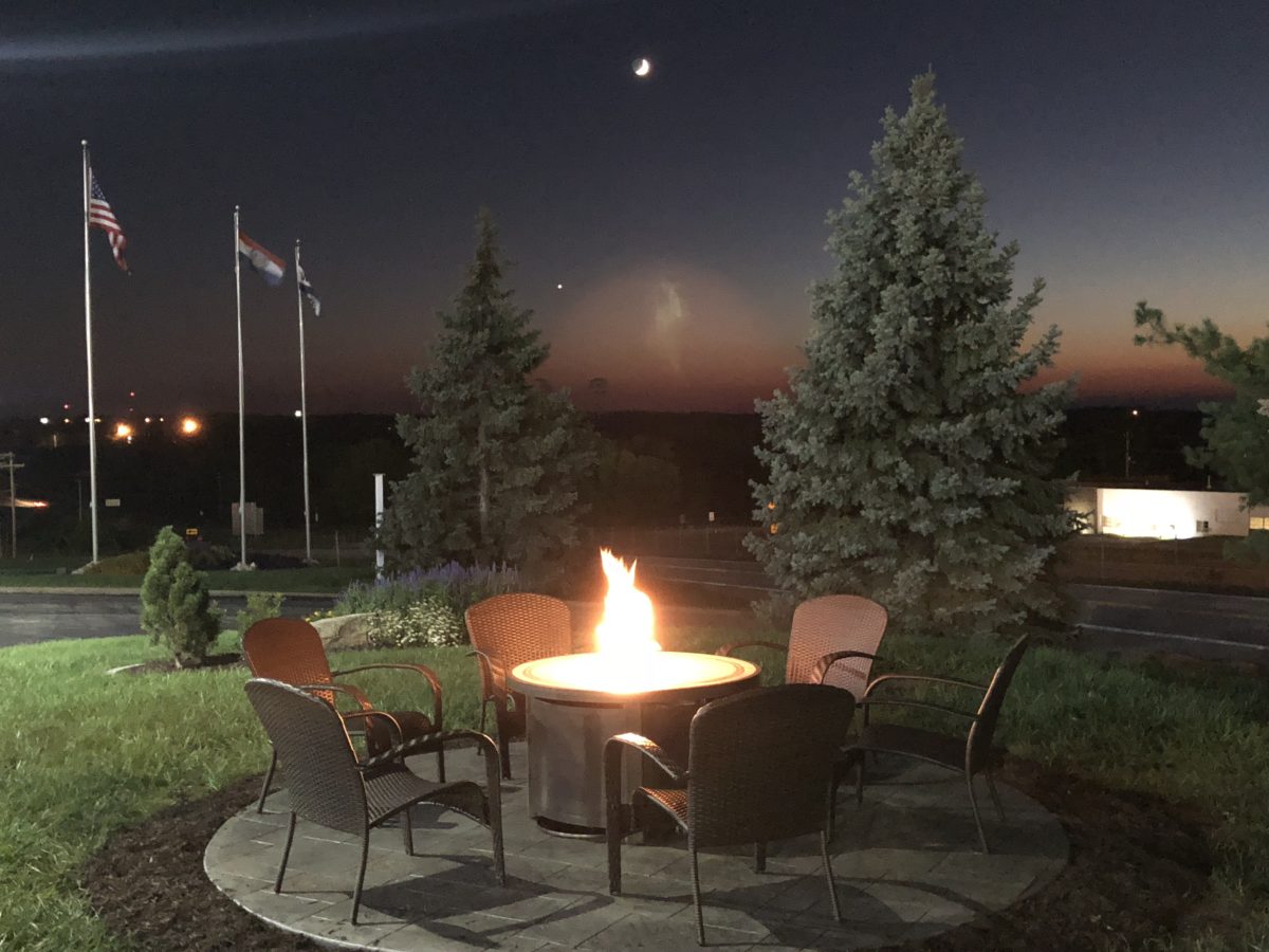 A lit fire pit with trees and chairs around it.