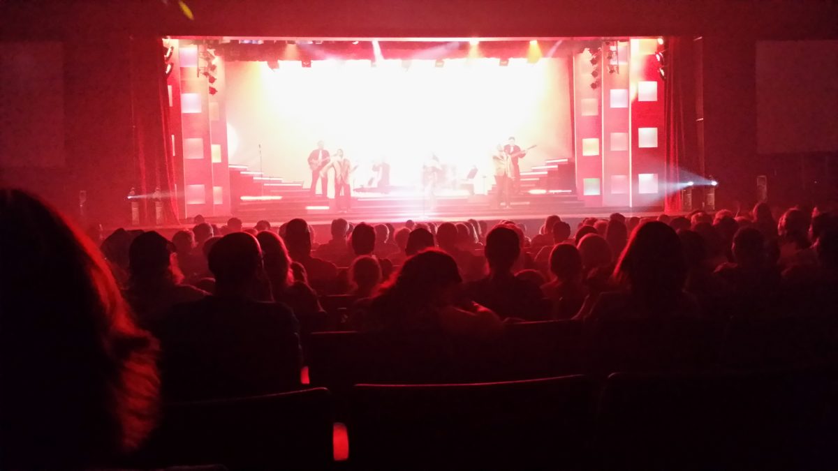 An audience watches a stage lit bright red.