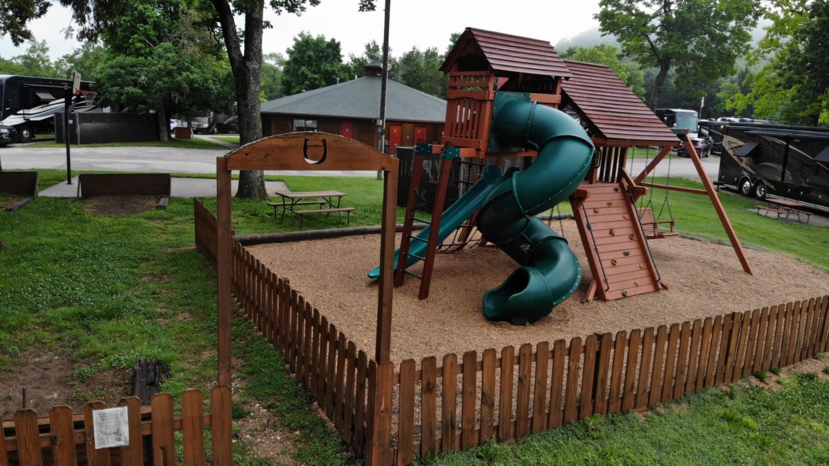 A small outdoor playground, including a winding green slide and rustic looking equipment.