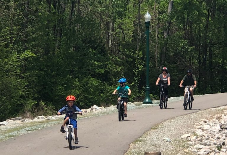 Several people in colorful helmets ride bikes down a paved path.