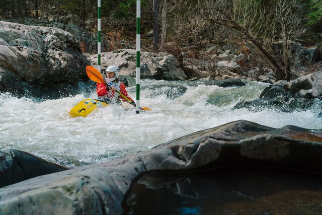 A woman paddles a kayak around large rocks and through rapids on the St. Francis River.