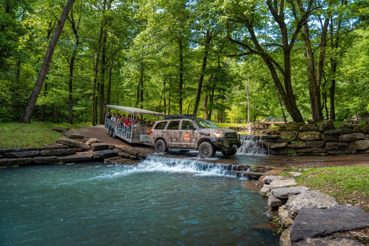 A tram is pulled by a truck over a creek.
