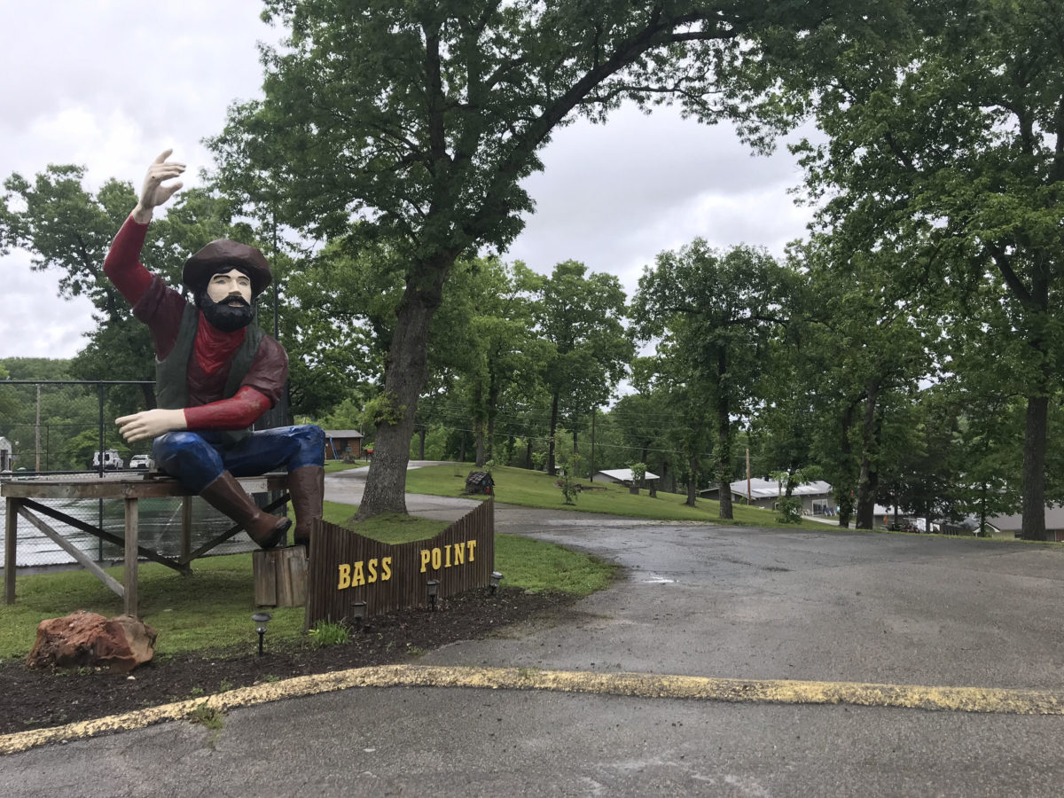 A large statue of a man waving beside the road.