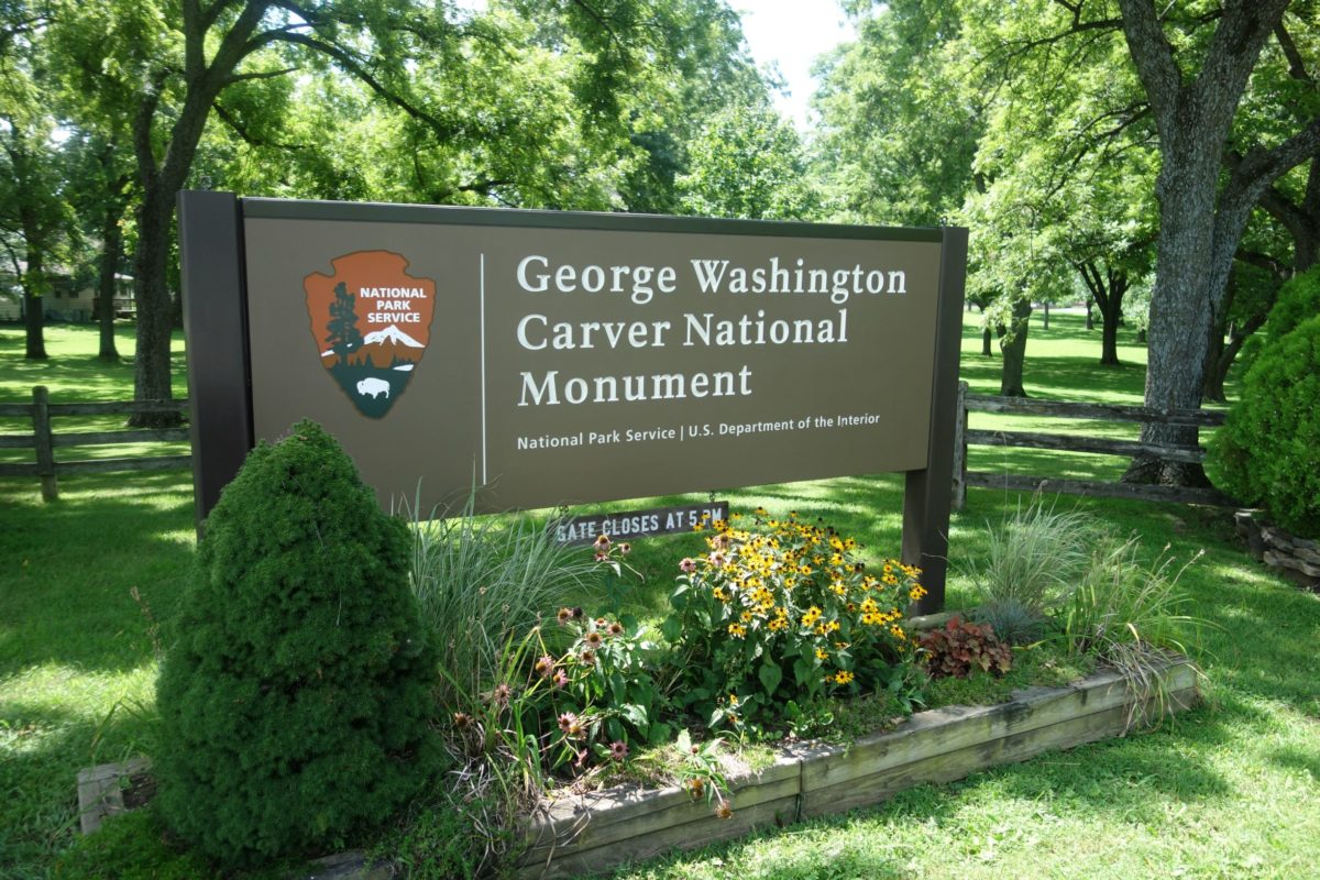 Park entrance sign surrounded by flowers and green plants.