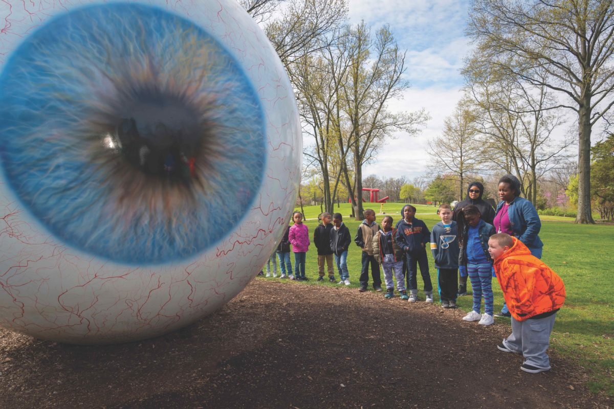 Group of younger students looking at Tony Tasset's "Eye" sculpture made of fiberglass, resin, oil paint, steel with a 452 inches circumference.