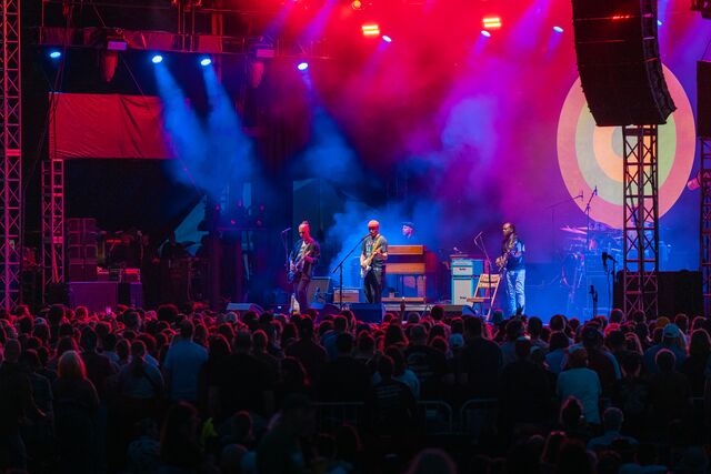 A band performs on a stage at night illuminated by red and blue spotlights.