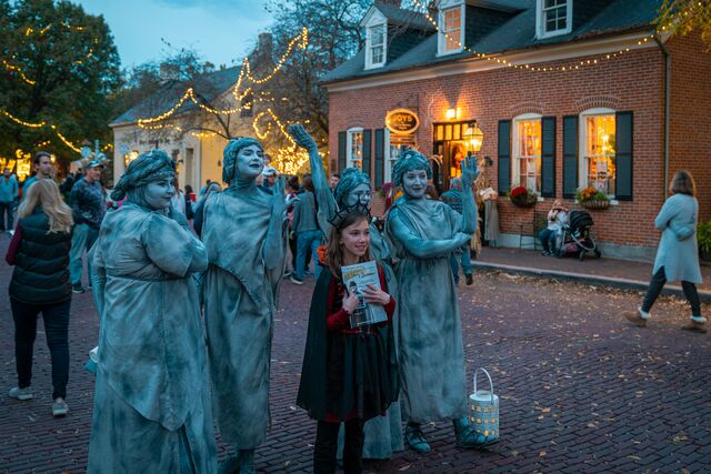 A girl poses with actors dressed as statues on a brick-lined main street that's decorated for fall.