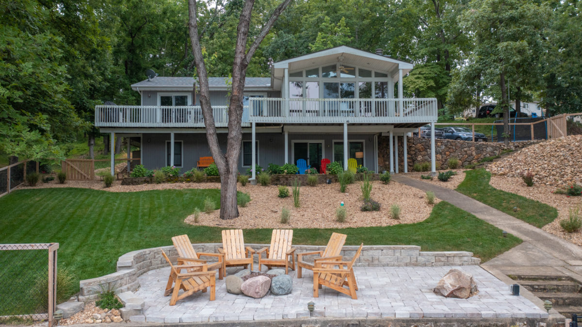 Chairs arranged on a dock before a lakeside house.