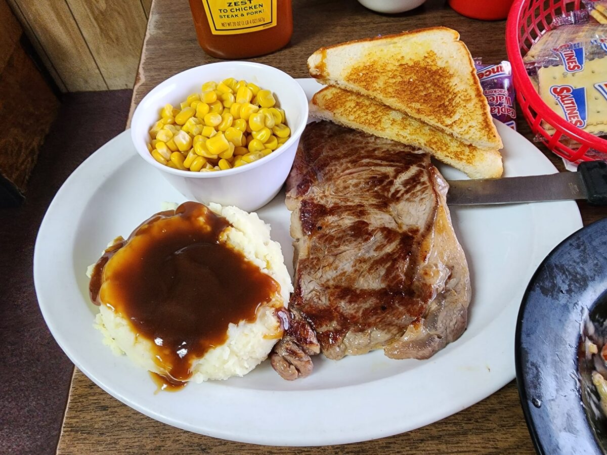 A plate with meat, mashed potatoes and gravy, toast and corn.