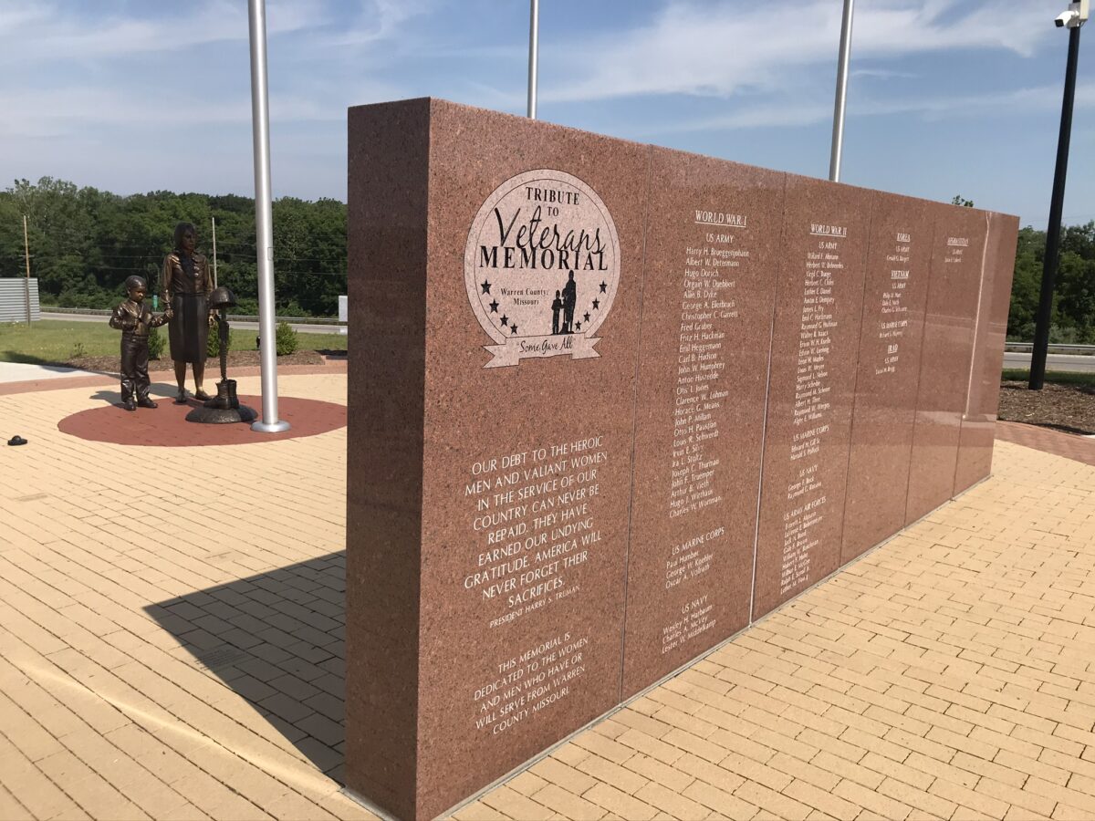 A red stone wall with the names of veterans etched onto it at a memorial.