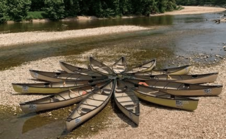 Several tan canoes arranged together in shallow water and on the shore.