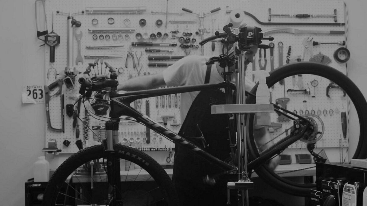 A black and white photo of a person working on a bicycle.