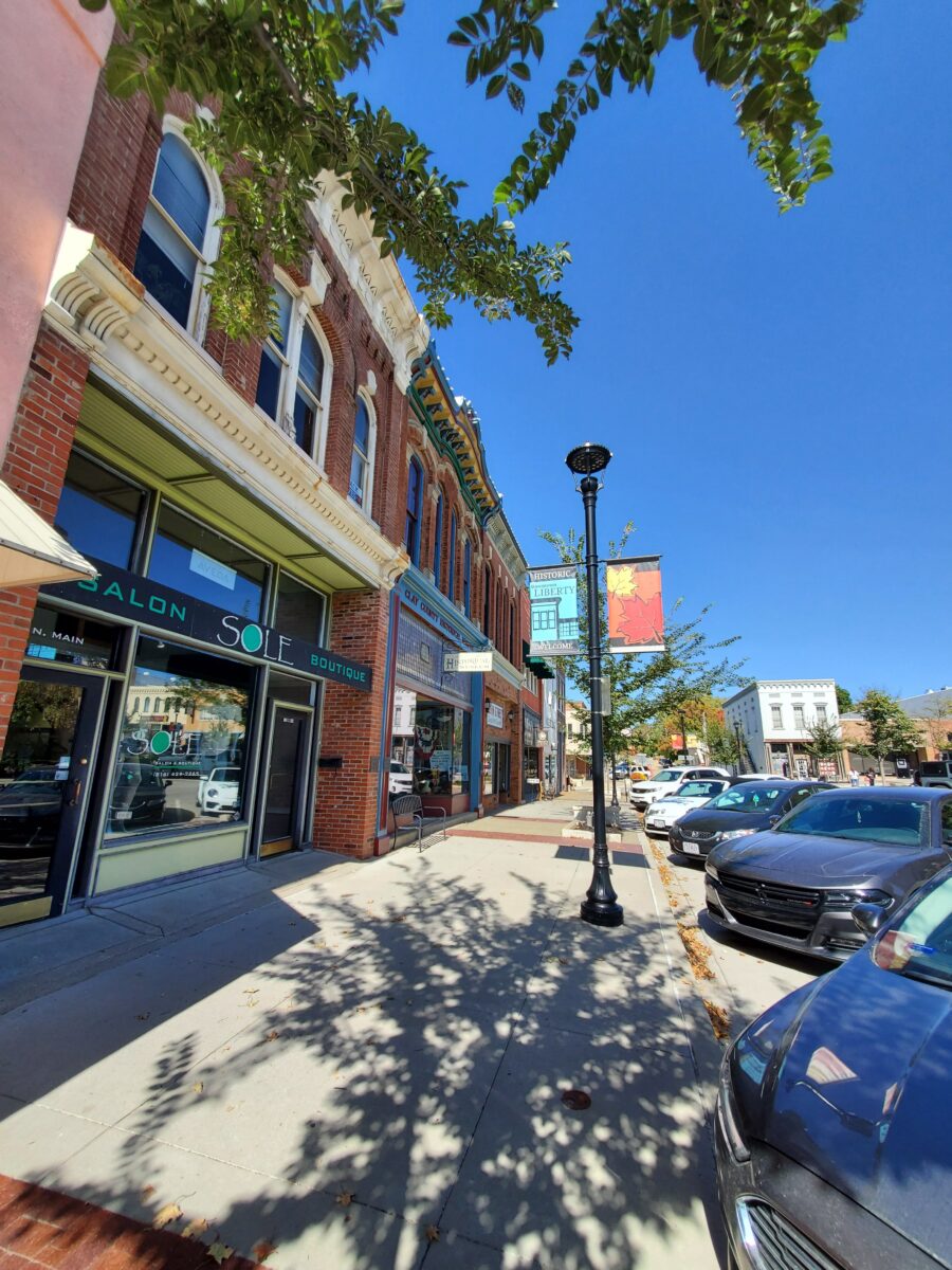 A city sidewalk with cars and shops.
