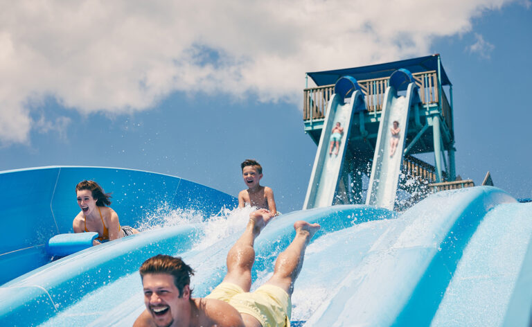 Three people go down the water slide with smiles on their faces at White Water.
