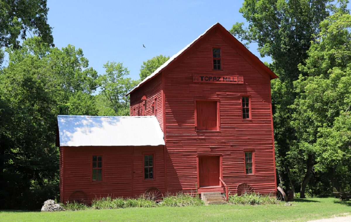 A red building sits amidst bright trees and grass.