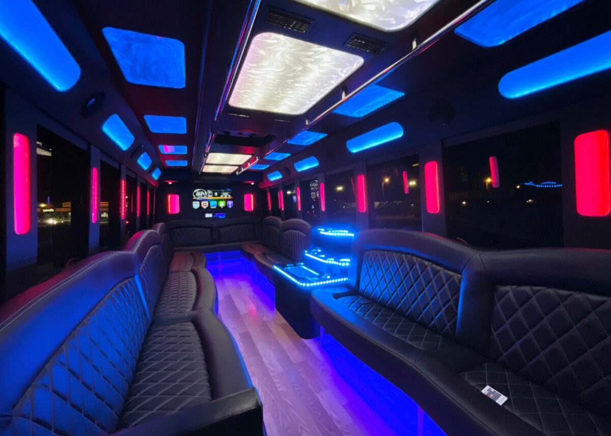 The inside of a party bus, lit with red and blue and outfitted with plenty of seating.