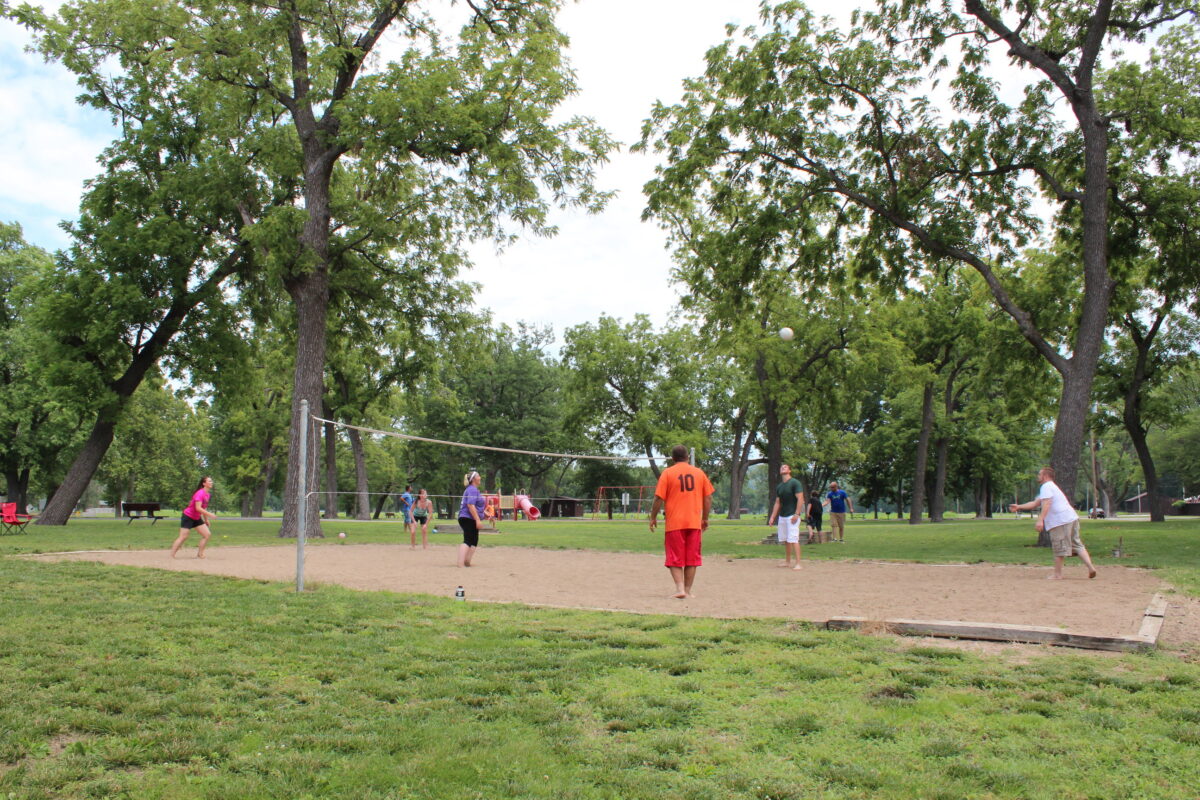 People playing volleyball on sand, with playground and trees and background