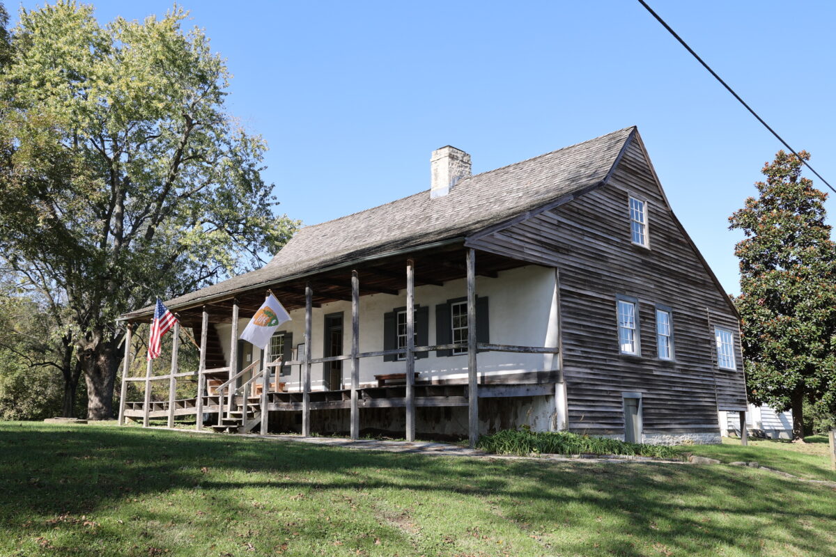 A house with a covered front porch, white front, plain wood siding and shingles.