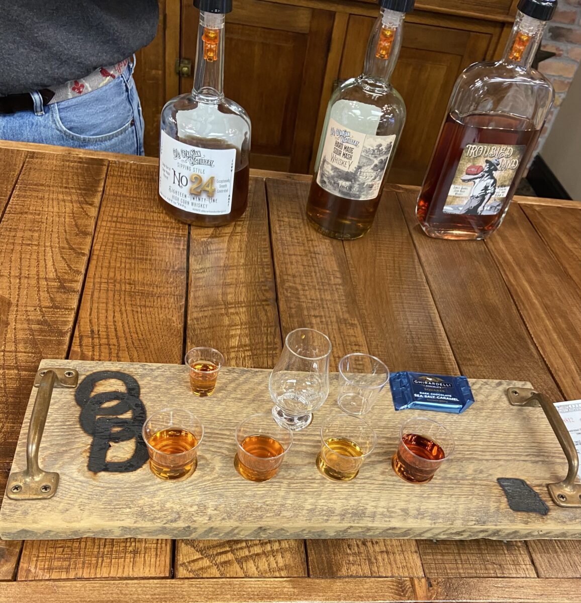Bourbon bottles and a tasting board of glasses on a table.