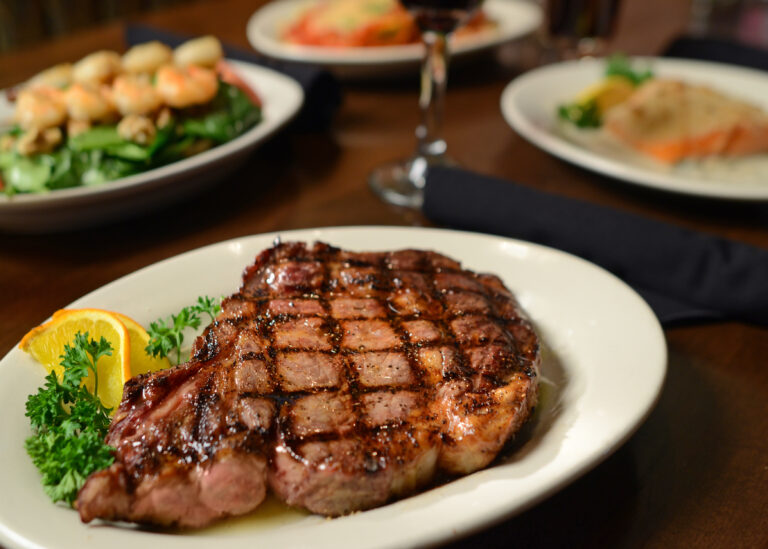 Ribeye steak with lemon and sprigs, plated on a table.