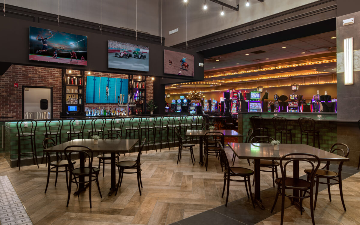 Interior view of Mark Twain Casino features a bar with flat-screen TVs, rows of slot machines and dining tables with chairs in the foreground and lining the bar.