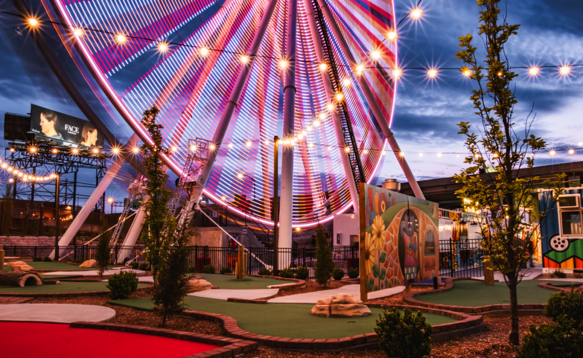 The bottom of a lit up Ferris wheel near other attractions.