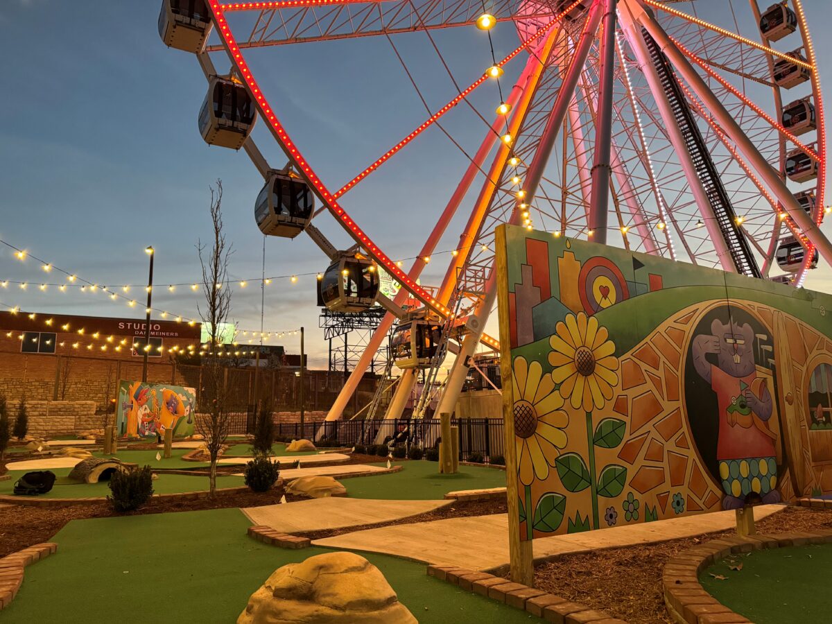 The bottom of a lit up Ferris wheel near other attractions.
