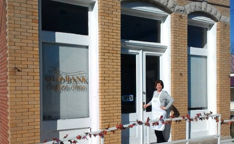 A woman stands outside of a coffee shop with brick exterior and a window decal.