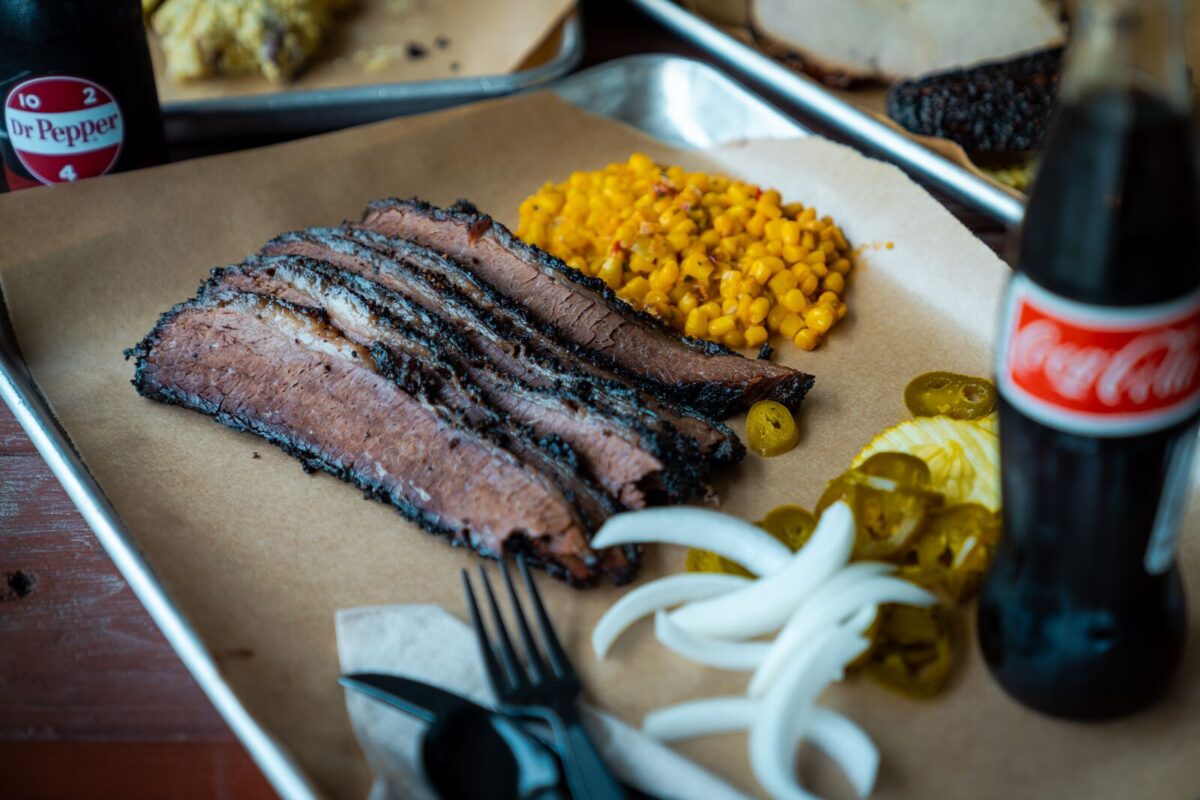 A metal tray sits on a table with slices of brisket, corn, onions and jalapenos.
